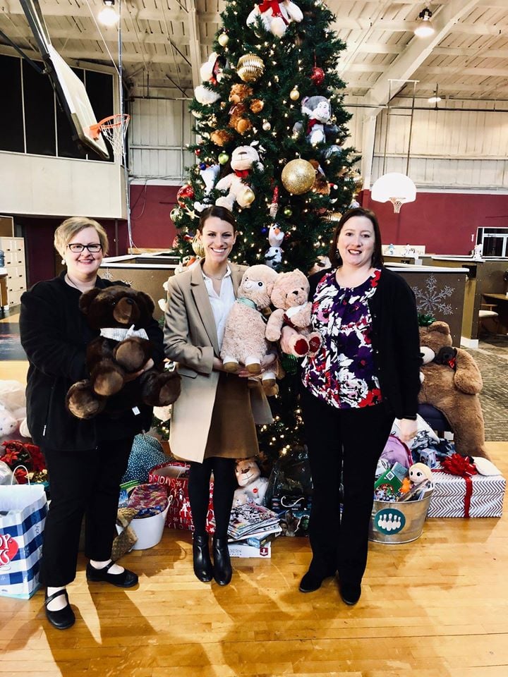 Three librarians hold stuffed animals in front of a Christmas tree.